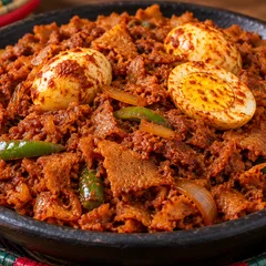 Firfir: shredded injera in berbere sauce with boiled eggs and green peppers in a black clay bowl