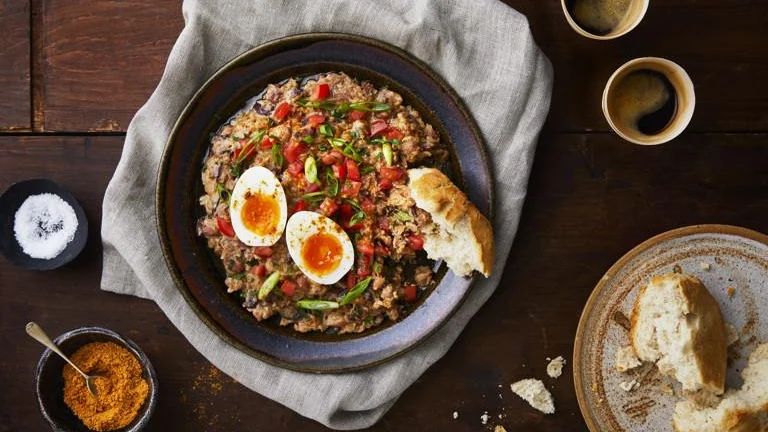 Ful: seasoned fava beans with chopped tomato, spring onion and soft-boiled eggs in a dark bowl, with bread
