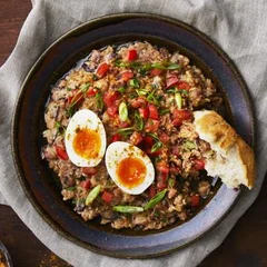 Ful: seasoned fava beans with chopped tomato, spring onion and soft-boiled eggs in a dark bowl, with bread
