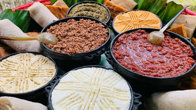 Kitfo and accompaniments in clay bowls with ayib and injera